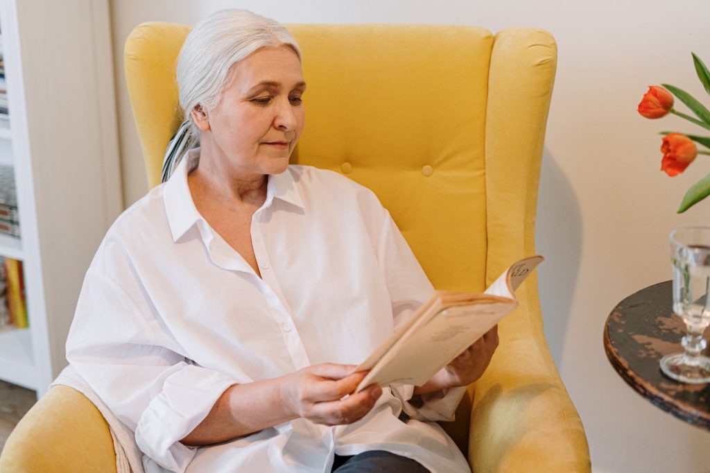 femme âgée en train de lire dans un fauteuil jaune